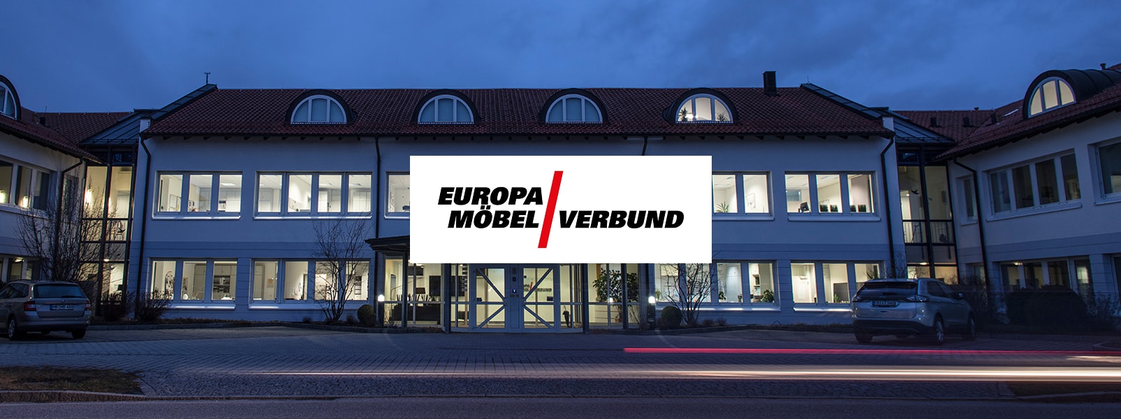 Fassade der Europa Möbel-Verbundgruppe bei Nacht mit beleuchtetem Logo