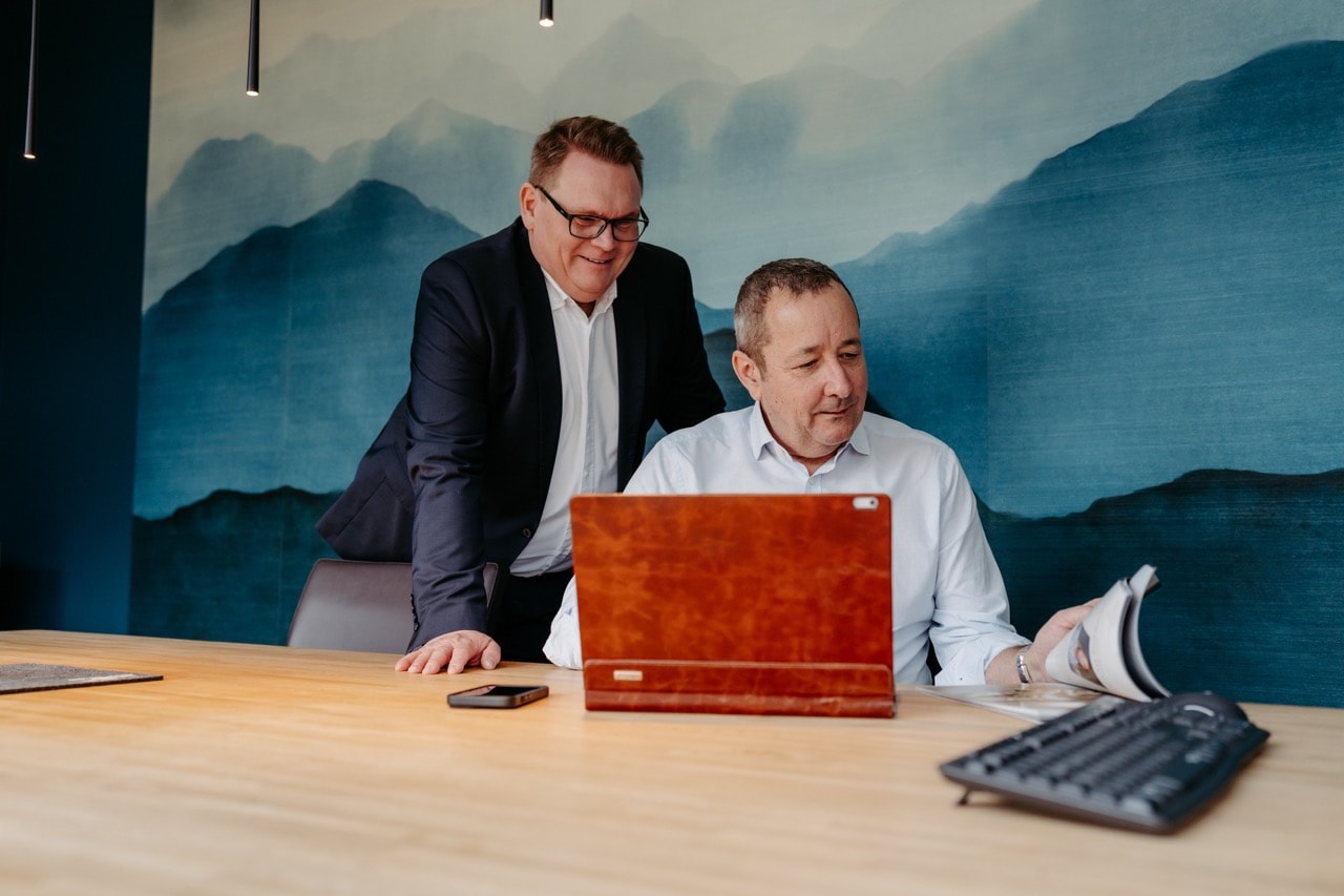 Alwin Justen und Stefan Tiemann gemeinsam am Laptop vor Bergkulisse-Tapete