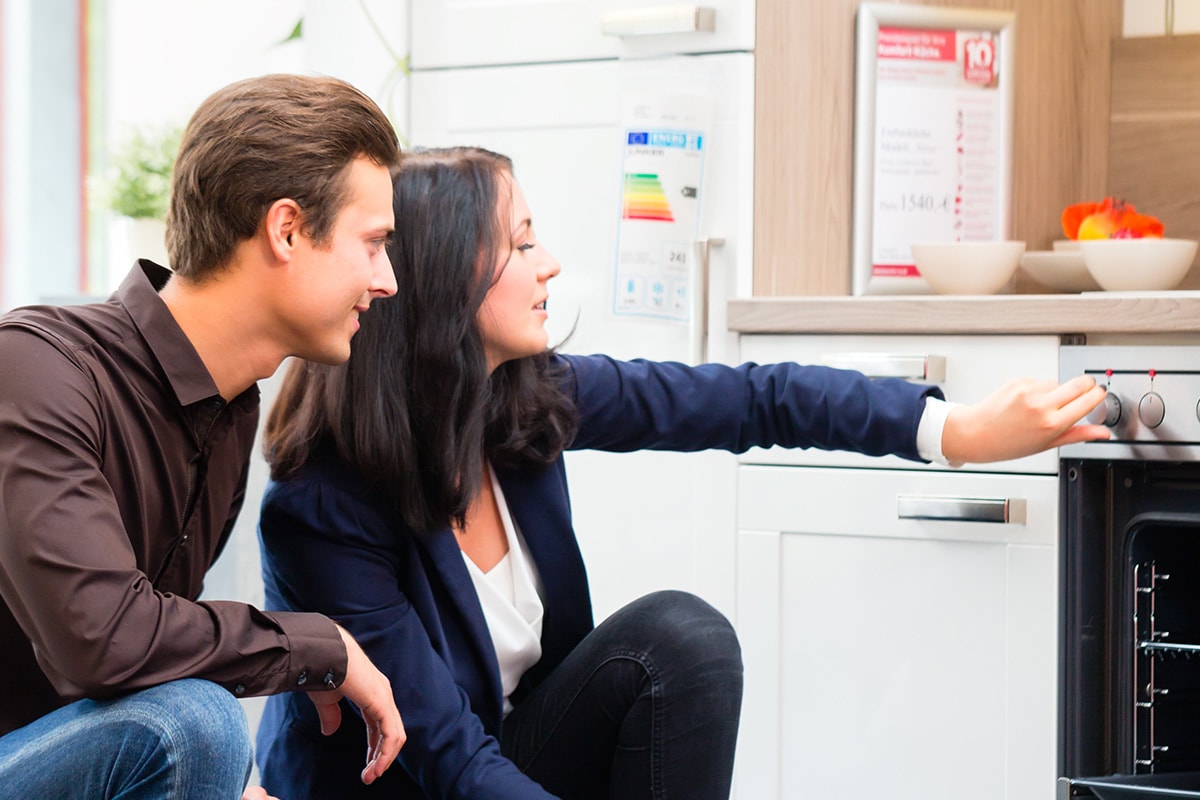 Junges Paar begutachtet lächelnd einen Backofen im Küchenstudio